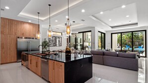 A modern kitchen with a large island, wooden cabinets, stainless steel appliances, and pendant lighting. - Luxe Retreat | 9BR Luxe Villa w/ Saltwater Pool, Gym, Theater, and Arcade Near Orlando Theme Parks (Kissimmee)