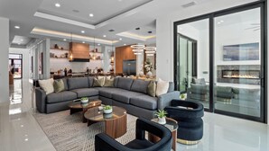 A modern living room with a sectional sofa, a coffee table, and a fireplace. - Luxe Retreat | 9BR Luxe Villa w/ Saltwater Pool, Gym, Theater, and Arcade Near Orlando Theme Parks (Kissimmee)