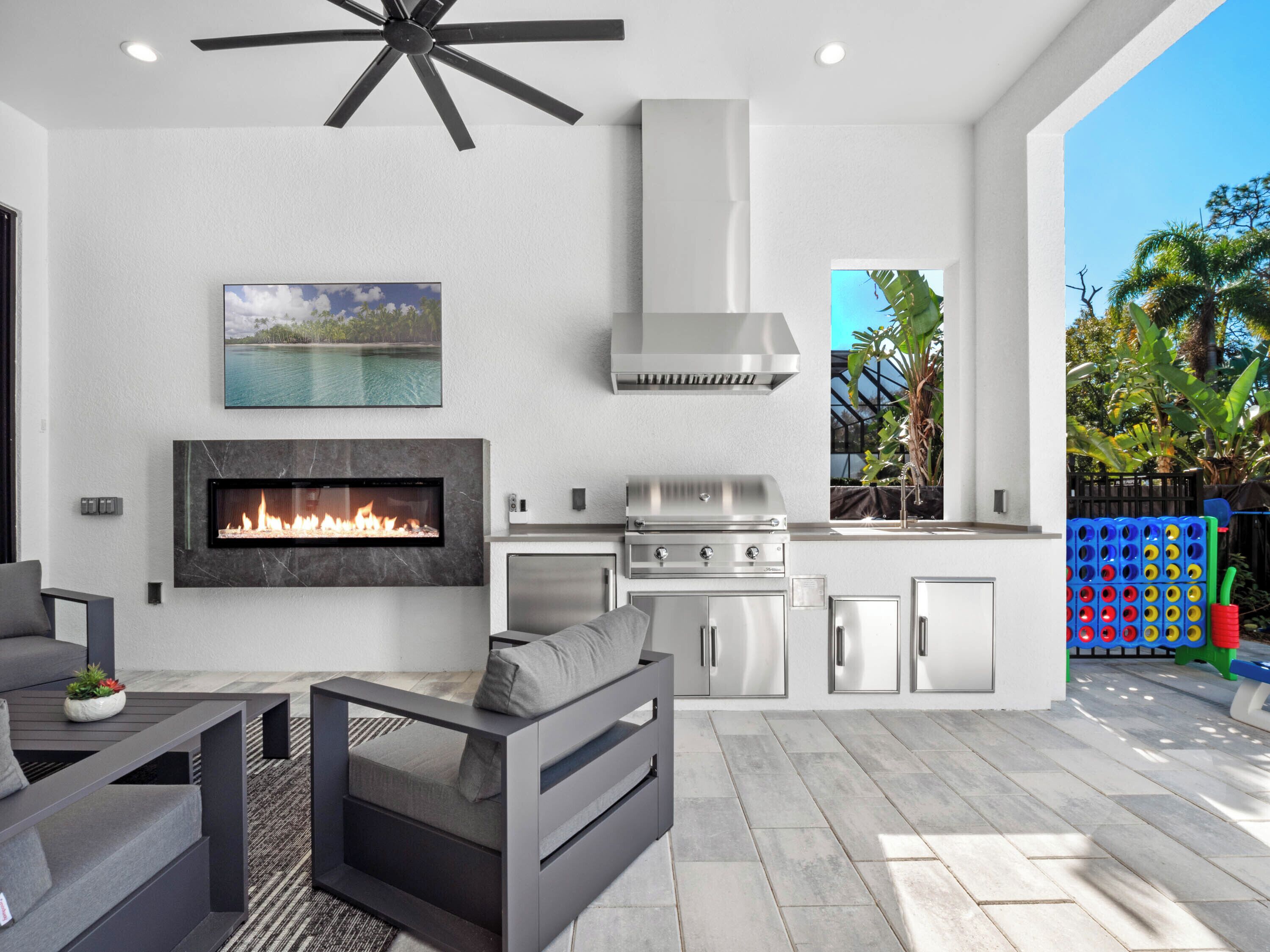 A modern outdoor kitchen with a built-in grill, a fireplace, and a dining area with a sofa and table.