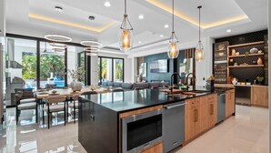 A modern kitchen with a large island, stainless steel appliances, and pendant lighting. - Luxe Retreat | 9BR Luxe Villa w/ Saltwater Pool, Gym, Theater, and Arcade Near Orlando Theme Parks (Kissimmee)