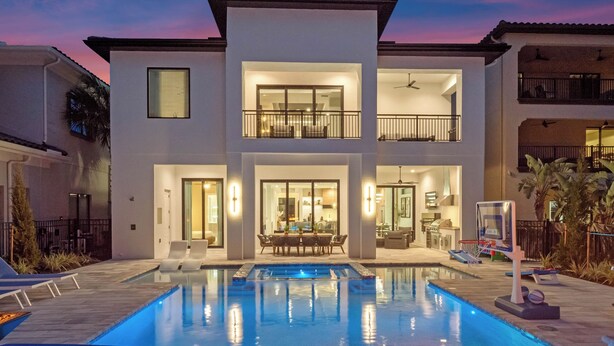 A modern two-story house with a swimming pool, outdoor seating, and a fire pit. - Luxe Retreat | 9BR Luxe Villa w/ Saltwater Pool, Gym, Theater, and Arcade Near Orlando Theme Parks (Kissimmee)