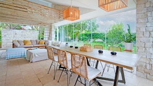 A spacious dining area with a long table, wicker chairs, and a stone wall backdrop.