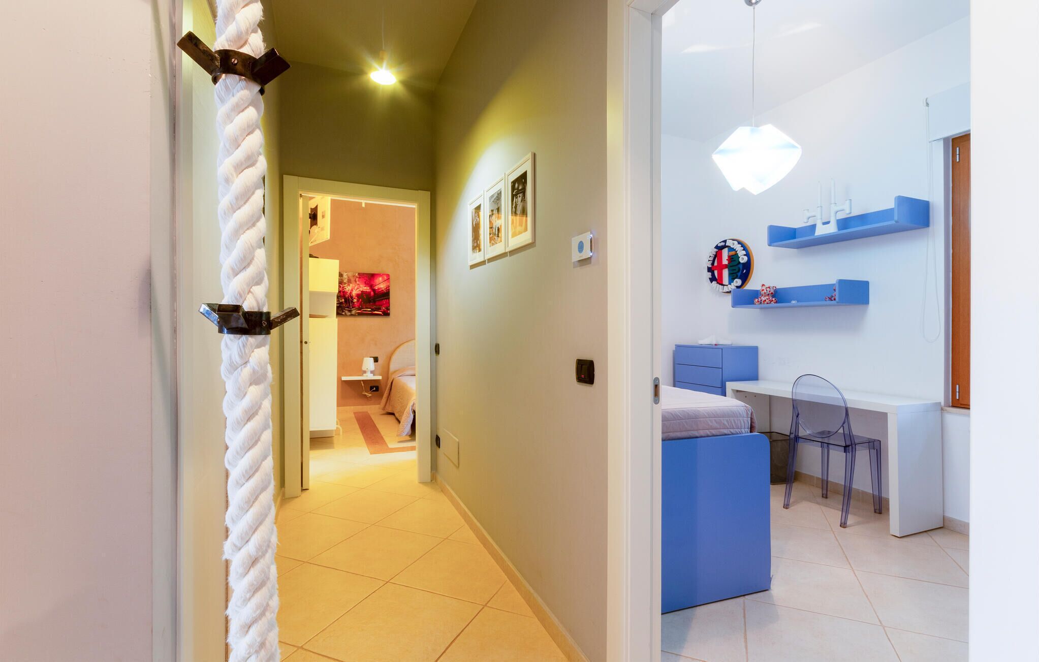 A hotel room with a bed, a desk, and a chair. There is a door with a rope handle leading to another room.