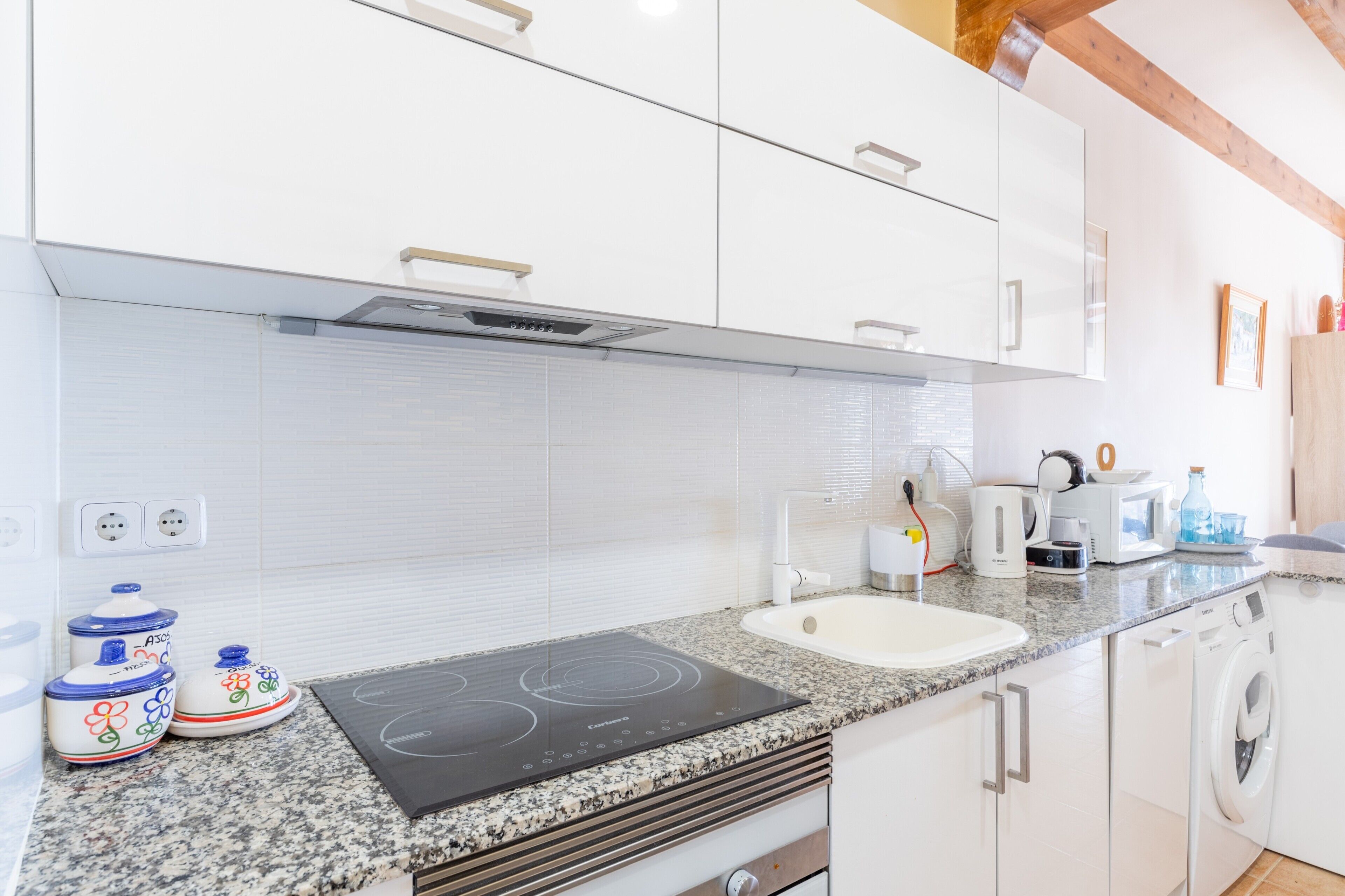 Una cocina moderna con armarios blancos, encimera de granito, estufa integrada, lavabo y lavadora.