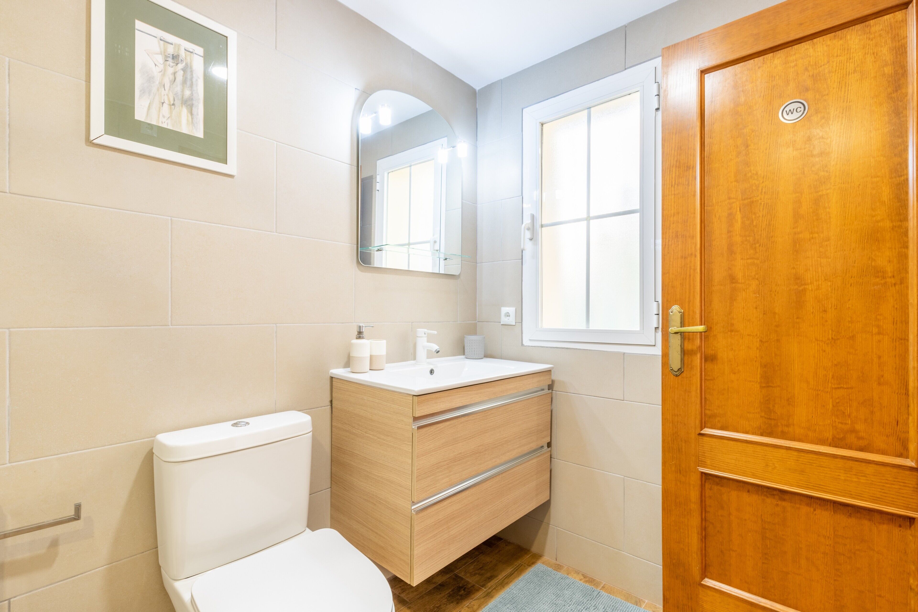 Une salle de bain comprenant des toilettes, un meuble-lavabo en bois avec un évier, un miroir et une porte en bois.