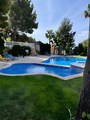 A swimming pool with lounge chairs, a stone wall, and a small building.