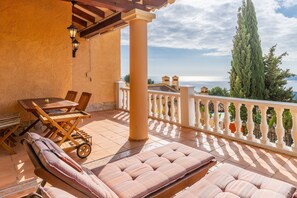 Eine sonnendurchflutete Terrasse im Freien mit Tisch, Stühlen und gepolsterten Sitzgelegenheiten.