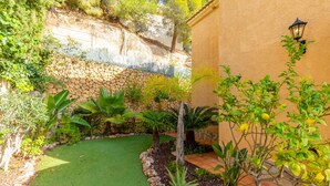 Un patio con pared de piedra, un pequeño césped y diversas plantas.