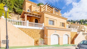 Un edificio de estilo mediterráneo con fachada de piedra, un balcón y un coche estacionado en la calle.