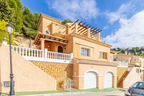 A Mediterranean-style building with a stone facade, a balcony, and a car parked in front.
