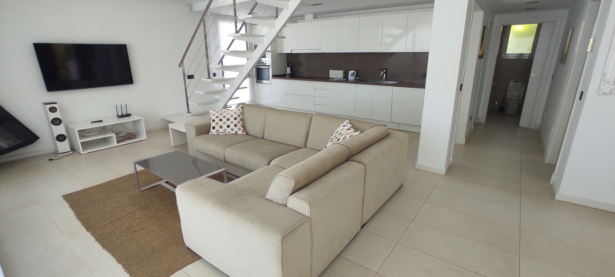 A modern living room with a sofa, a coffee table, a TV, and a staircase leading to a kitchen.