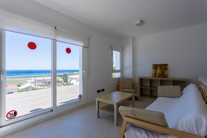 Una habitación con cama, una silla, una mesa y vistas al océano a través de amplios ventanales.
