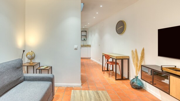 A modern living room with a sofa, a TV, a dining table with chairs, a kitchen in the background, and a clock on the wall. - Holiday Home 'La Reine' with Wi-Fi and Air Conditioning (Béziers)