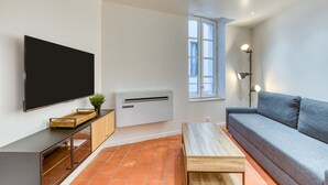 A modern living room with a flat-screen TV, air conditioning unit, sofa, and a small table. - Holiday Home 'La Reine' with Wi-Fi and Air Conditioning (Béziers)