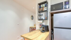 A compact kitchen with a wooden table, a coffee maker, a refrigerator, and a shelf with decorative items. - Holiday Home 'La Reine' with Wi-Fi and Air Conditioning (Béziers)