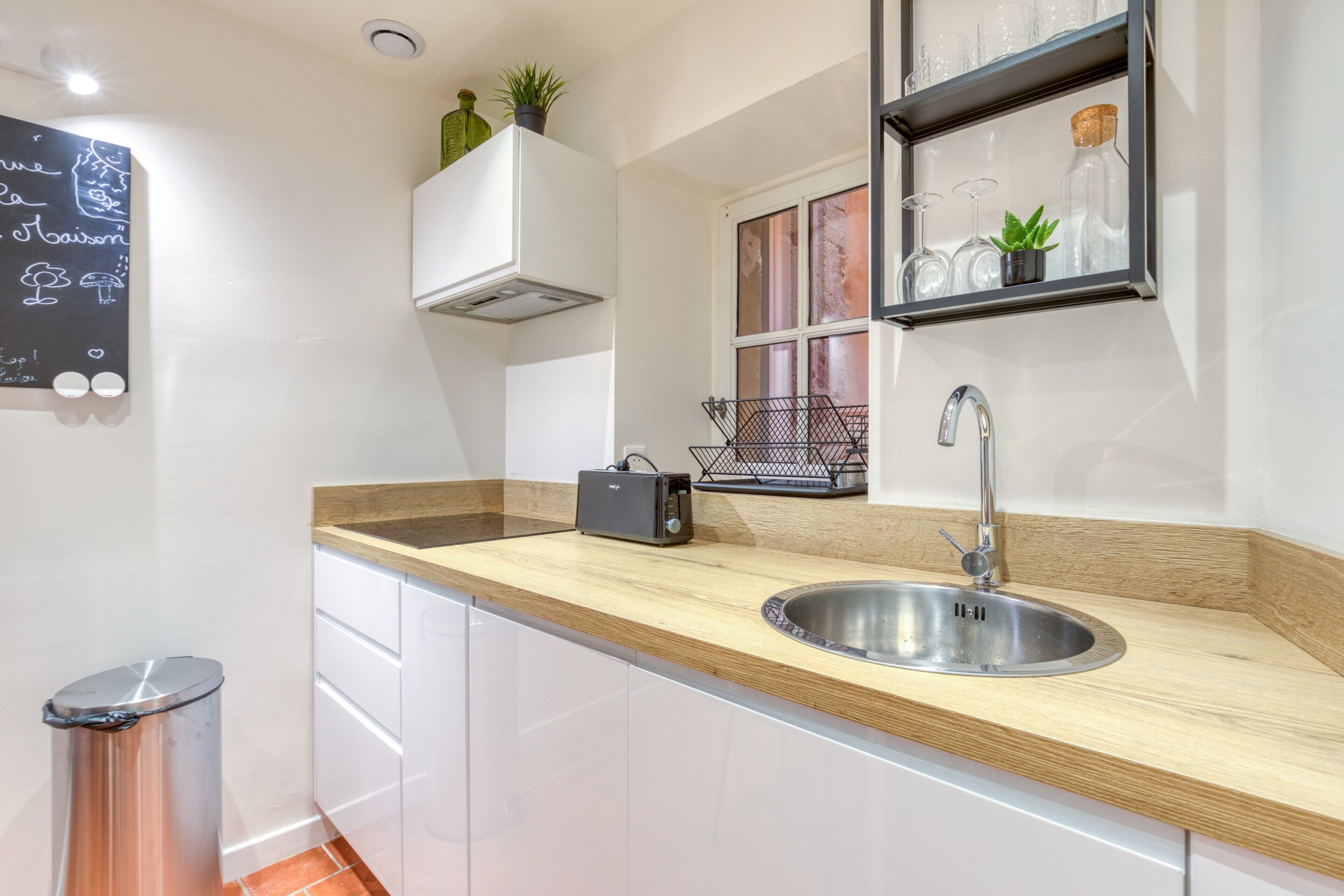 A modern kitchen with a wooden countertop, stainless steel sink, and a chalkboard with writing.