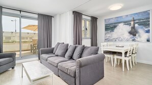 Un saló modern amb un sofà gris, una taula de cafè blanca i una zona de menjador amb caires blanques i una taula.