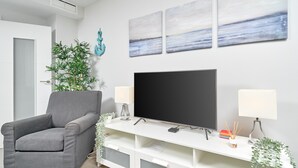 Un saló amb una poltrona gris, televisió plana, moble blanc per a l'electrònica i obra d'art a la paret.