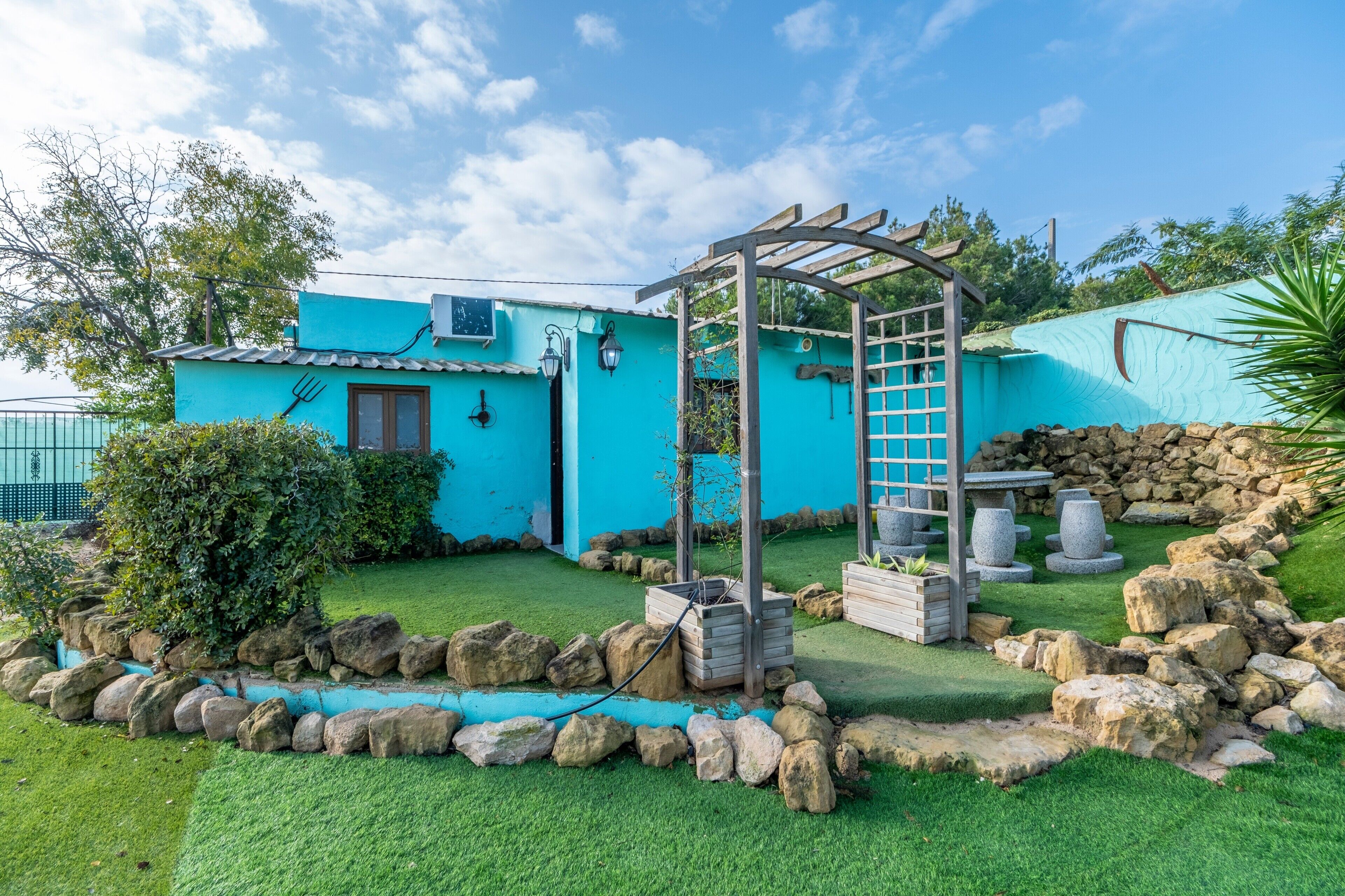 Un edificio azul con pérgola, muro de piedra y jardín de rocas.