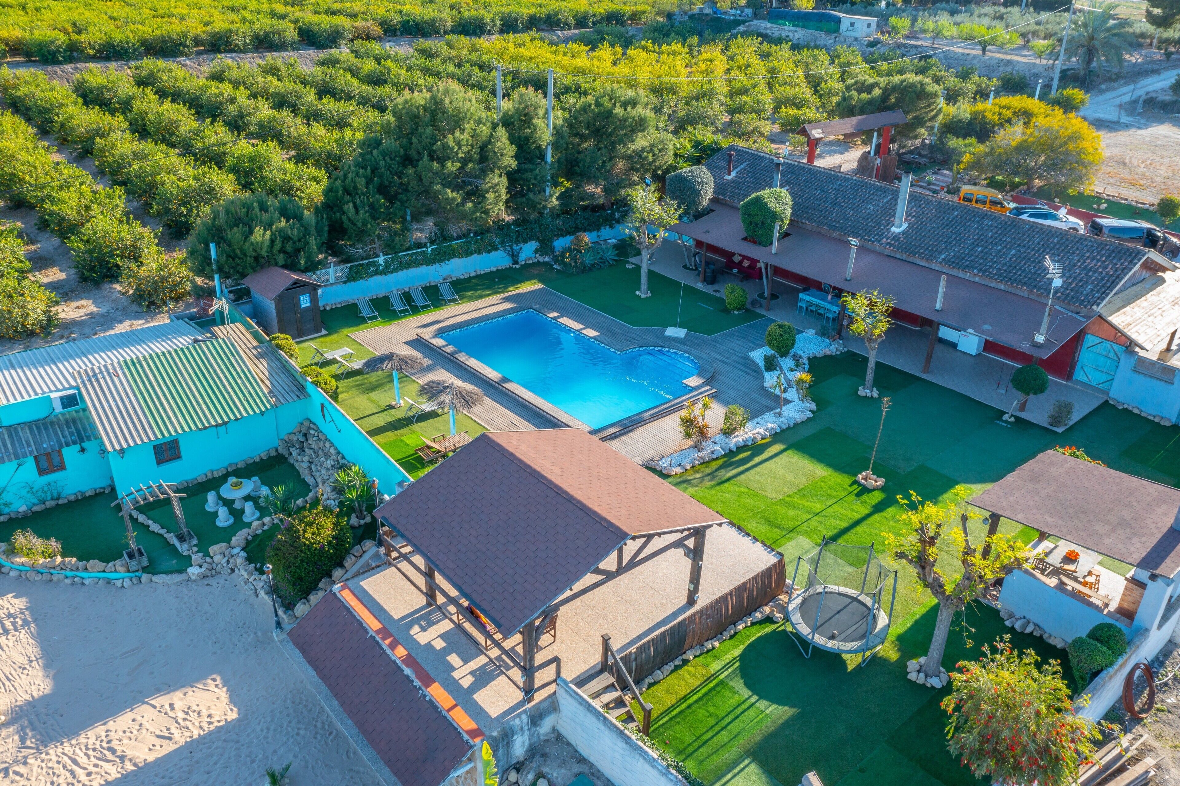 Vista aérea de una propiedad con piscina, césped verde y un edificio pequeño con techo rojo.