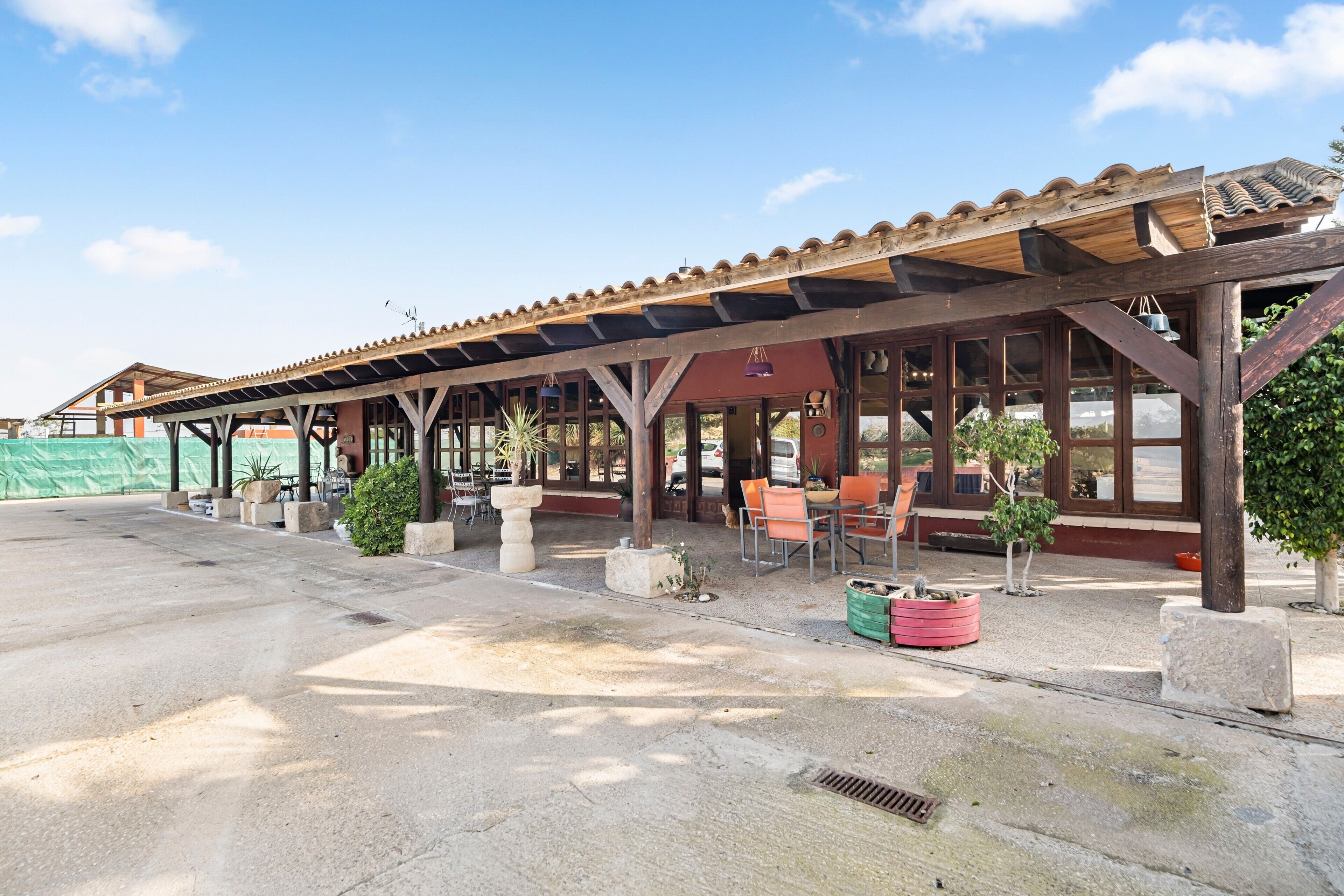A covered outdoor seating area with tables and chairs, potted plants, and a clear sky.