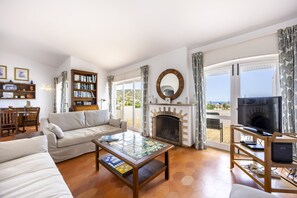 Een woonkamer met een bank, een salontafel, een open haard, een televisie en een boekenkast.