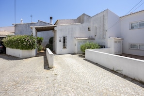 A white building with a tiled roof, a small garden area, and a paved courtyard. - Casa das Buganvilias 2LBC by Coolhouses (Luz)