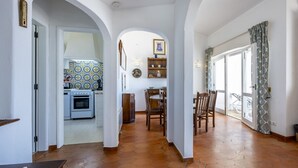 Une cuisine spacieuse avec un mur recouvert de carreaux, un coin repas avec une table et des chaises, et une vue dégagée grâce à une porte ouverte.
