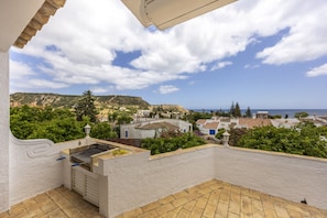 A balcony with a grill, a view of a coastal town, and a clear sky. - Casa das Buganvilias 2LBC by Coolhouses (Luz)