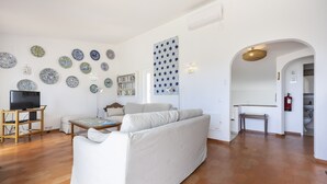Ein Wohnzimmer mit einer Couch, einem Fernseher auf einem Lowboard, einem Bücherregal und einer Wand mit Muster.