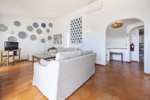 A living room with a sofa, a TV on a stand, a bookshelf, and a patterned wall. - Casa das Buganvilias 2LBC by Coolhouses (Luz)