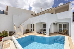 Eine moderne Villa mit Swimmingpool, Sitzgelegenheiten im Freien und einer Treppe zum Obergeschoss.
