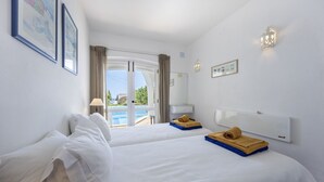 Une chambre d’hôtel avec deux lits, une grande fenêtre, une vue sur la piscine et un mur blanc orné de tableaux.