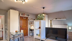 A modern living room with a glass dining table, a flat-screen TV, and a bookshelf. - Casa Curro — Cozy Studio with Garden Views in Baena (Baena)