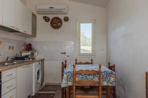 Cocina compacta con lavadora, una mesa de comedor con mantel floral y ventana con vistas.