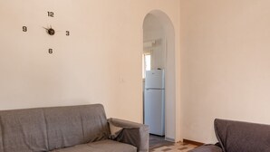 Una sala de estar con un sofá, un reloj en la pared y un acceso a una cocina.