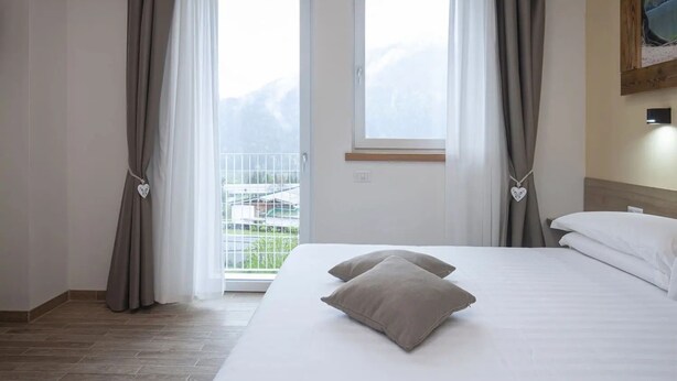 A hotel room with a bed, curtains, a window, and a painting on the wall.