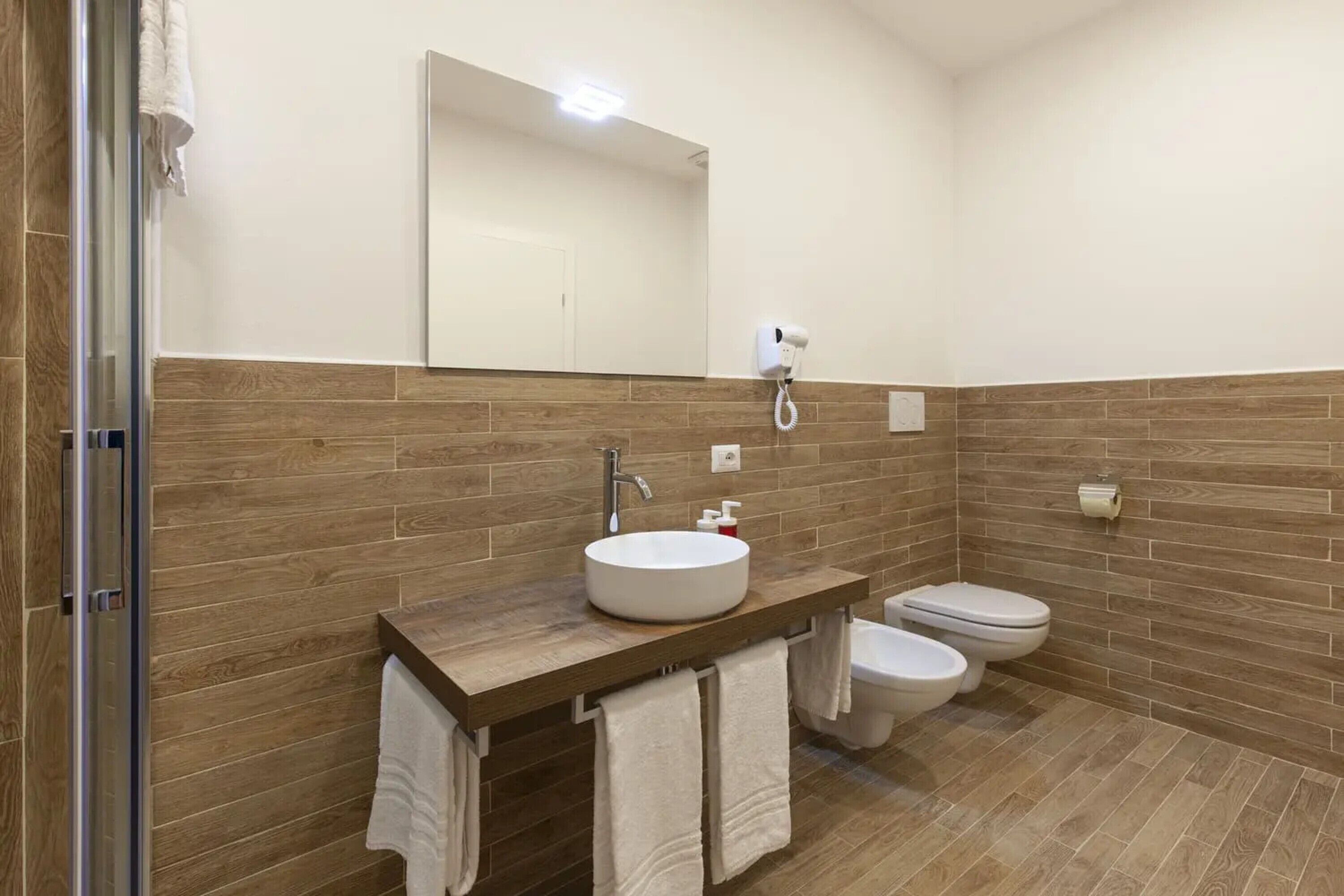A bathroom with a wooden vanity, a sink, a toilet, and a shower area.