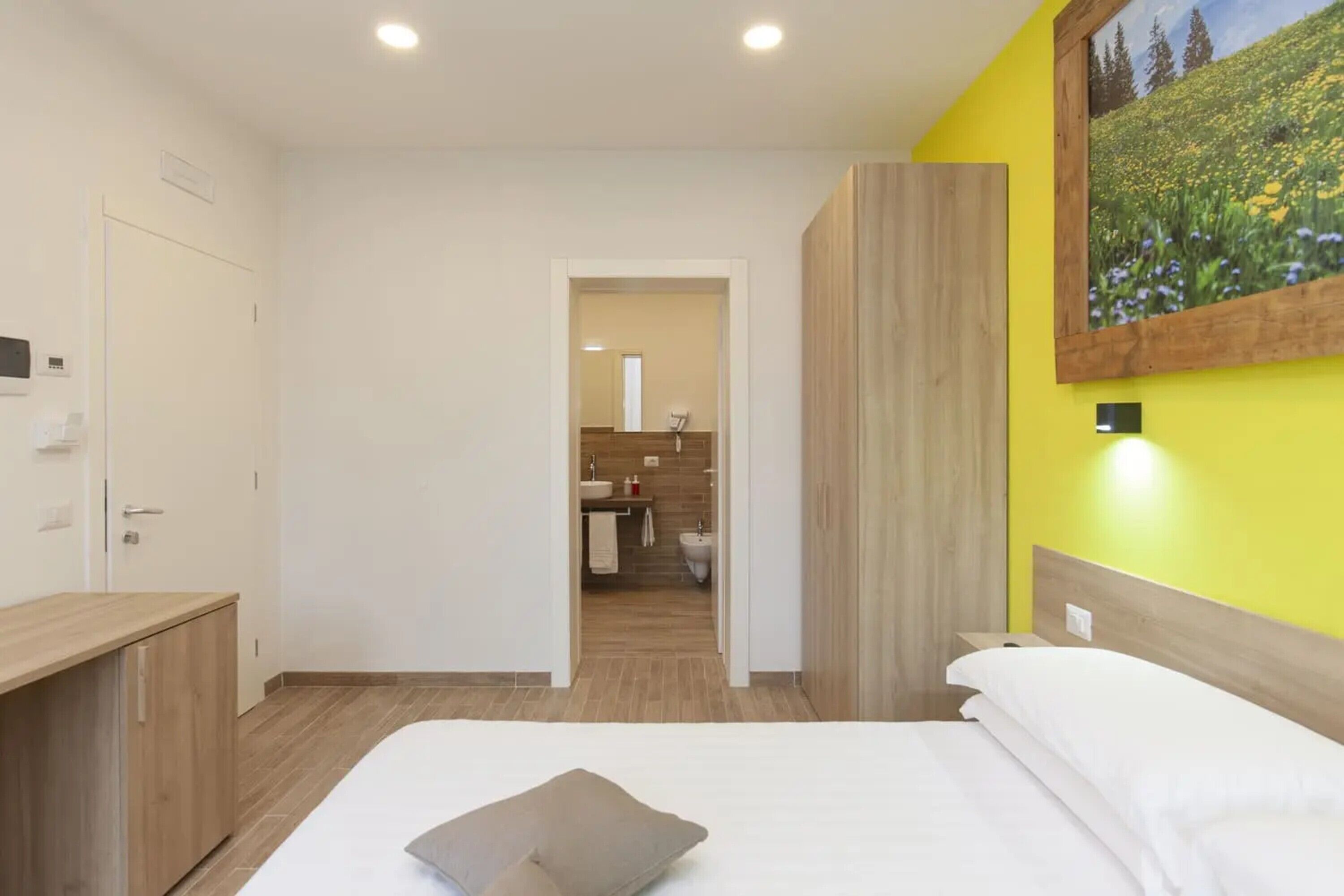 Une chambre à coucher avec un lit, une table de chevet, une armoire en bois et une salle de bain visible à travers une porte ouverte.