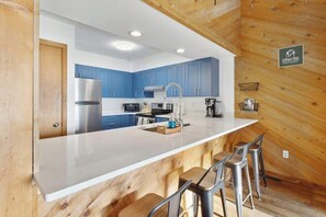A modern kitchen with blue cabinets, a stainless steel refrigerator, and a bar area with stools.