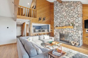 Una sala moderna con chimenea de piedra, un sofá, una mesa de centro, y una cocina visible a través de una puerta abierta.