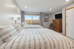 A bedroom with two beds, a wooden wardrobe, a television, and a window with a view. - Shanty Creek Retreat! (Bellaire)