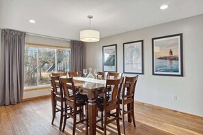 A dining area with a wooden table and chairs, a chandelier, and framed pictures on the wall. - Shanty Creek Retreat! (Bellaire)
