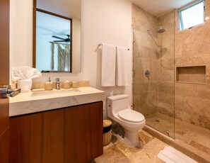 A modern bathroom with a marble sink, a toilet, and a glass-enclosed shower. - NHOA 306A 2BR Top Jungle View Aldea Zama (Tulum)