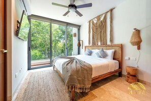 Un dormitorio con cama, ventilador de techo, ventana grande y un tapiz de macramé en la pared.