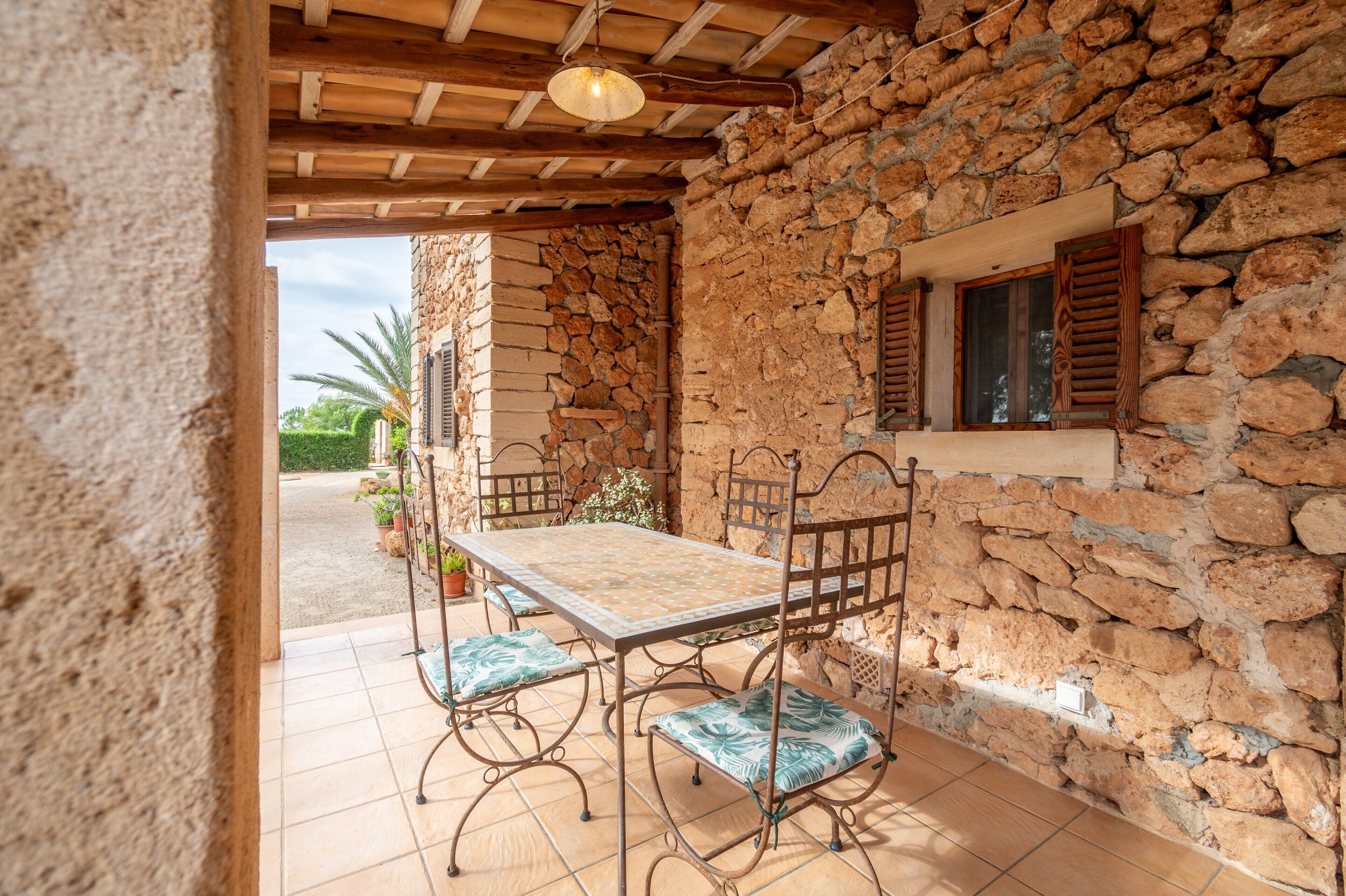 Eine Terrasse mit Steinwänden, einem Tisch und Stühlen, einer Holzbeschichtung und einem Fenster mit Fensterläden.