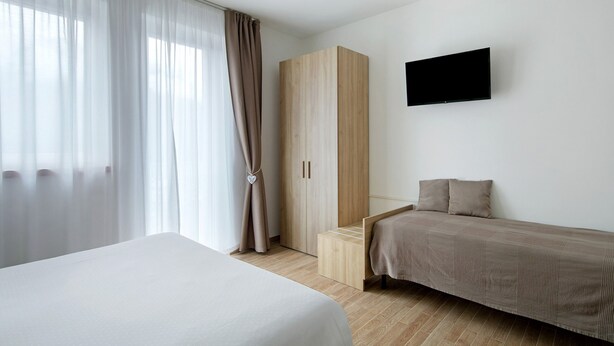 Une chambre à coucher avec un lit, une armoire, une télévision et une fenêtre avec des rideaux.