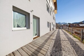 En bygning med træterrasse, dør og et vindue med gardin.