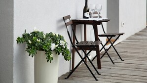 Een houten terras met een tafel, stoelen, een plant in pot en een fles wijn.