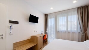 Een hotelkamer met een bed, een bureau met stoel, een aan de muur bevestigde televisie en een raam met gordijnen.